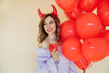 A young woman with red horns and heart-shaped balloons and a gift box. The March 8 holiday and Valentine's Day.