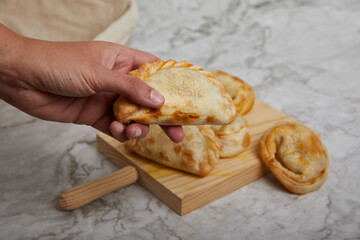 Argentinean Empanadas on a wooden board on a marble table. Hand holding an empanada.