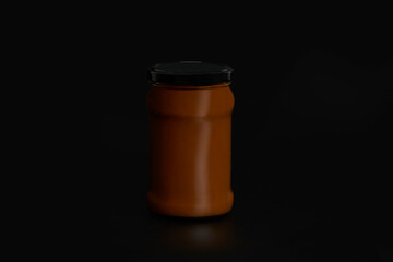 Unbranded dulce de leche jar with black lid on black endless background and reflection below.