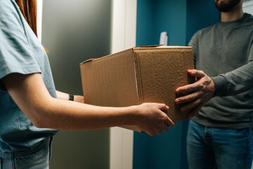 Close-up cropped shot of woman customer receiving cardboard box parcel at home from delivery man...