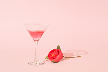 Martini glass and camellia flower on pink pastel background. Minimal party concept. Top view, copy space.