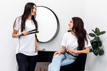 Young beautiful woman discussing hairstyling with her hairdresser holding iron while sitting
