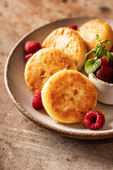 Syrniki closeup with honey topping and raspberry and mint on ceramic plate on brown textured background