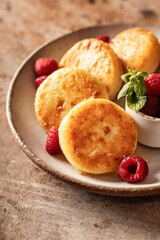 Cottage cheese pancakes, syrniki closeup with honey topping and raspberry and mint on ceramic plate on brown textured background