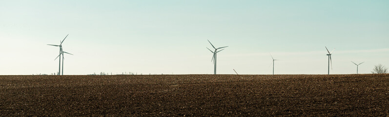 Shovel stuck in the middle of the field. Wind turbines rise behind the field. It's a beautiful...
