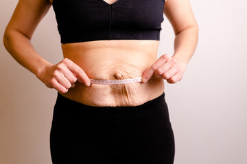cropped woman dressed in black top and black leggings measure Diastasis with Measuring Ruler