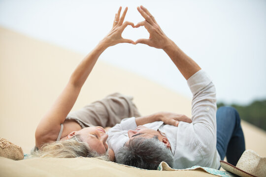 mature couple making heart with their hands on beach