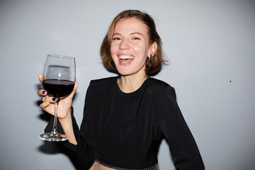 Portrait of carefree young woman partying and holding wine glass while looking at camera, shot with...