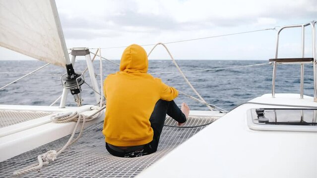 Tourist photographer man in a yellow sweatshirt on a yacht looking at the ocean and making picture