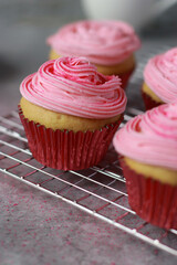 Close up of vanilla muffins with pink frosting on top, grey marble table and white stone wall in background