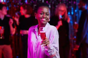 Waist up portrait of smiling African American woman holding drink at party in neon lights, copy...