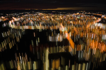 Abstract motion blurred effect of aerial view of buildings and bright illuminated streets in city residential area at night. Dark urban landscape at high altitude