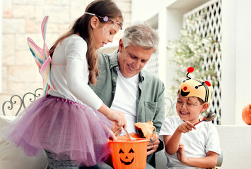 We all love halloween. Shot of two adorable young siblings carving out pumpkins for Halloween with their grandfather at home.