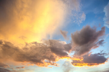 Dramatic sunset landscape with puffy clouds lit by orange setting sun and blue sky.