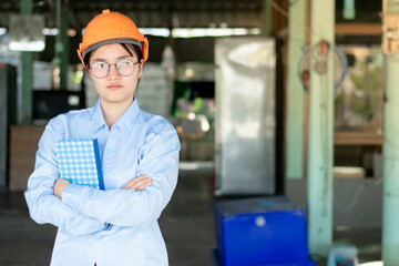 An Asian female engineer stands holding a book and has a copyspace.