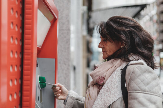 Mature Brunette Woman With Credit Card In Hand Near Automated Teller Machine In Shop