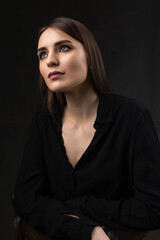 Portrait of a young brunette with long hair in the studio. Dramatic photo in dark colors.