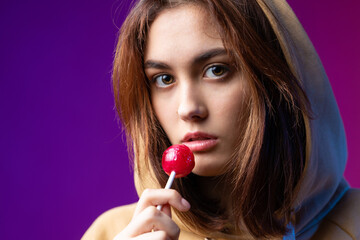 Portrait of a woman in a hoodie, girls licking a red round lollipop with beautiful makeup on a...