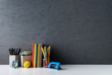 Creative desk with a blank picture frame or poster space, desk objects, office supplies, books, and plant on a dark blue background.