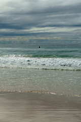 Fototapeta na wymiar View of sand, surf, sea and overcast cloudy sky, with a single person swimming. Currumbin Beach, Queensland, Australia 