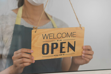Owner business retail, asian young woman hand in turning sign board to open coffee shop, wearing face mask protect to pandemic of coronavirus, reopen store after close lockdown quarantine in covid-19.