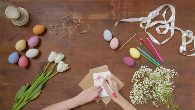 Top view of a table with items to create a composition for Easter. A woman's hand writes with a red marker: April 24. Christ is risen. Church holiday-Easter