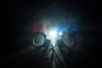 Police raid at night and you are under arrest concept. Silhouette of handcuffs with police car on...