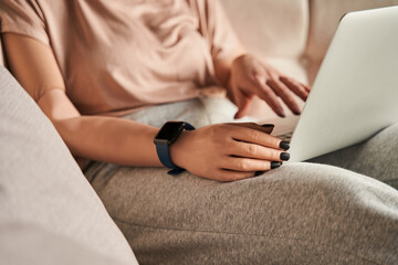 Woman with prosthesis limb sitting at the sofa and using laptop while woking or relaxing at home