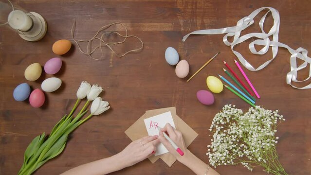 Top view of a table with items to create a composition for Easter. A woman's hand writes with a red marker: April 17. Christ is risen. Church holiday-Easter