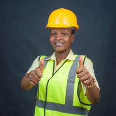 African Nigerian female construction or civil engineer, architect or builder with yellow safety helmet and green reflective jacket, doing thumbs up gestures