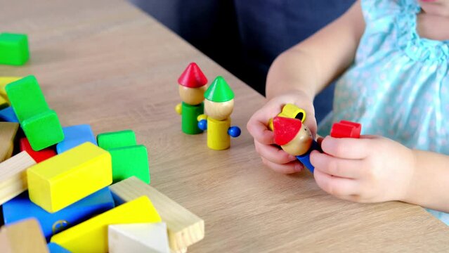 close-up of children's educational toys in hands of toddler, small child, a 2-year-old girl builds houses for characters from color blocks, concept of childhood, earlier child development, creativity