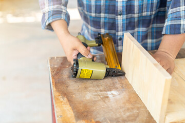 The carpenter using nail gun to nail wood board.