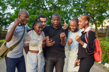 Groups of african friends, students or sport lovers consisting of male and female individuals, happily staring into the smart phone with various jubilation gestures and expressions © kehinde