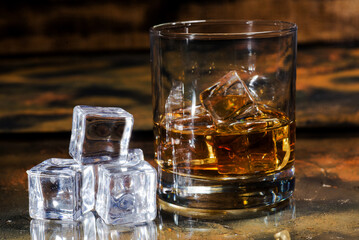 glass of whiskey with ice cubes on a glass brown table with reflection.