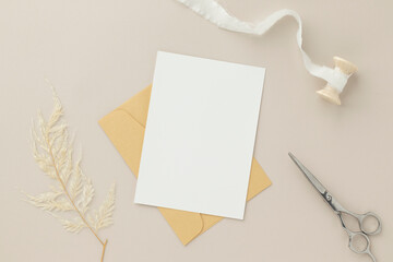 Blank greeting card invitation Mockup 5x7 on Brown envelope with dried flowers on beige background, flat lay, mockup