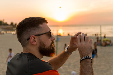 Man photographing sunset on the beach with smartphone