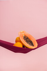 two oranges and a papaya cut in half on a red cloth in front of a peach background as a symbol of the pelvic floor