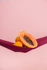 two oranges and a papaya cut in half on a red cloth in front of a peach background as a symbol of...