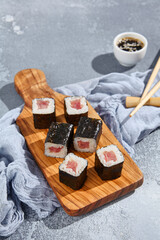 Hosomaki roll with tuna on wooden board in contemporary composition. Simple sushi roll with tuna on concrete table. Maguro hosomaki in minimal style.