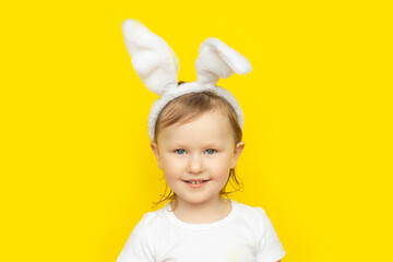 Happy little girl with bunny ears on yellow background