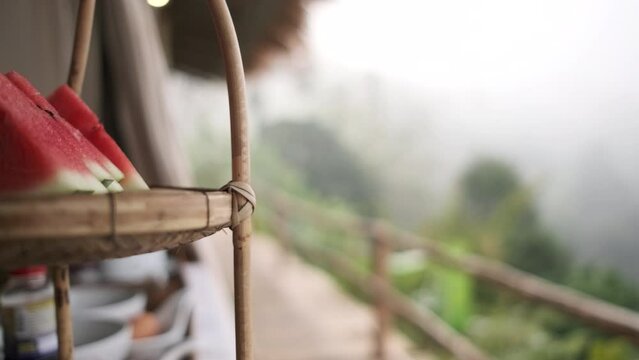 Pan footage of rural natural scenic from wooden terrace of traditional craft bamboo tourist resorts in Chaing Mai, Thailand, winter breakfast in fog, fresh watermelon at mountain view landscape.