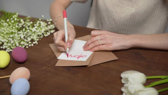 Close-up on a table with items to create a composition for Easter. A woman's hand writes with a red marker: April 24. Christ is risen. Church holiday-Easter