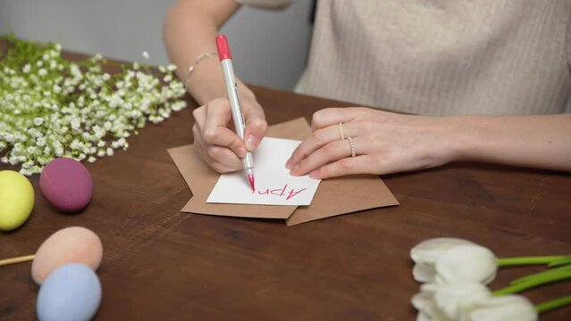 Close-up on a table with items to create a composition for Easter. A woman's hand writes with a red marker: April 17. Christ is risen. Church holiday-Easter