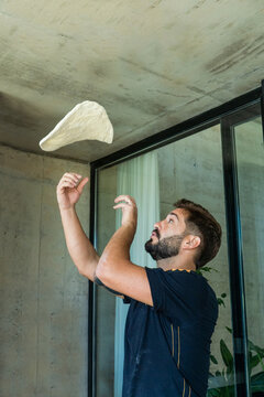 Young Man Stretching Pizza Dough By Throwing It In The Air