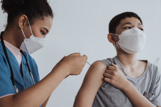 Asian Boy In Medical Face Mask Getting Vaccine Shot By Doctor. Kid Getting Vaccinated From Doctor And Nurse To Prevent Coronavirus. Covid-19 Vaccination Campaign In A Clinic.