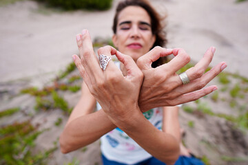 Latin female holds fingers in mudra gesture while meditates at the beach receiving spring season....