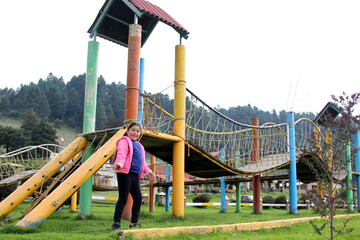 Latin little girl with long straight black hair, overweight body positive and does sports playing in the playground in the middle of the forest and mountains with trees
