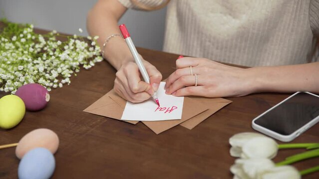 Close-up on a table with items to create a composition for Easter. A woman's hand writes with a red marker: Happy Easter. Christ is risen. Church holiday-Easter