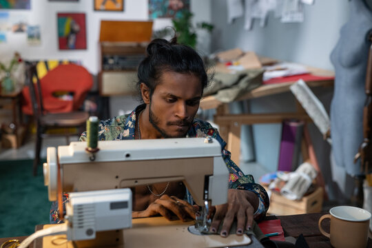 Young creative fashion designer bending over electric sewing machine and creating new seasonal collection in workshop - Powered by Adobe