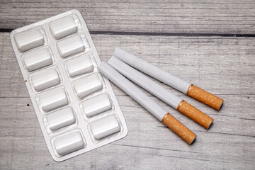 A blister pack with nicotine gum and three cigarettes on a wooden background as a symbol of smoking cessation